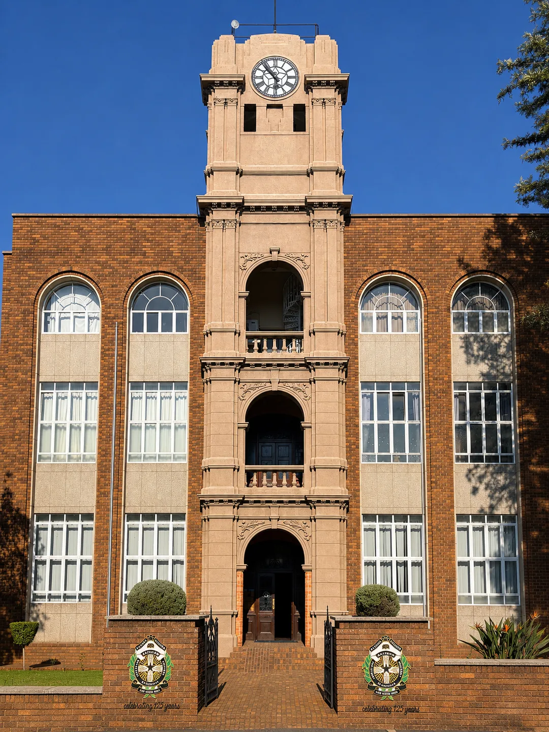 Close-up view of the War Memorial Clock Tower at St Patrick’s CBC Kimberley, showing its ornate stone-coloured façade, clock face, arched entrances and balconies, set against a clear blue sky.