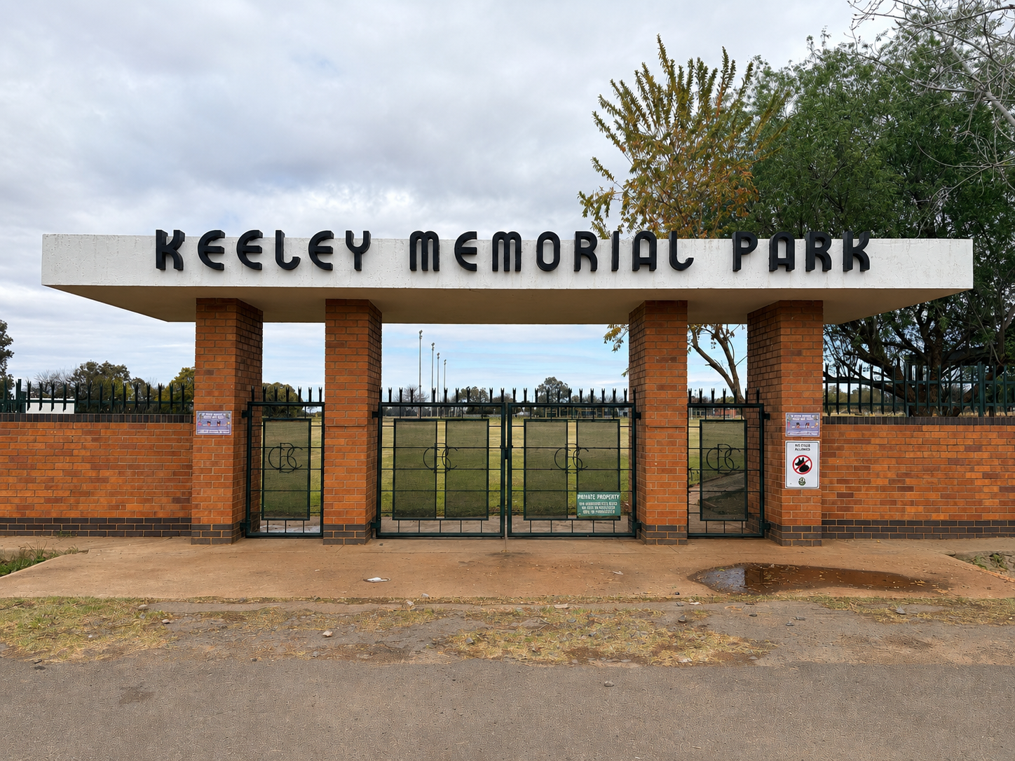 Entrance to Keeley Memorial Park in Kimberley, showing the large white entrance canopy with the words “Keeley Memorial Park”, brick pillars, green gates and the sporting fields beyond.