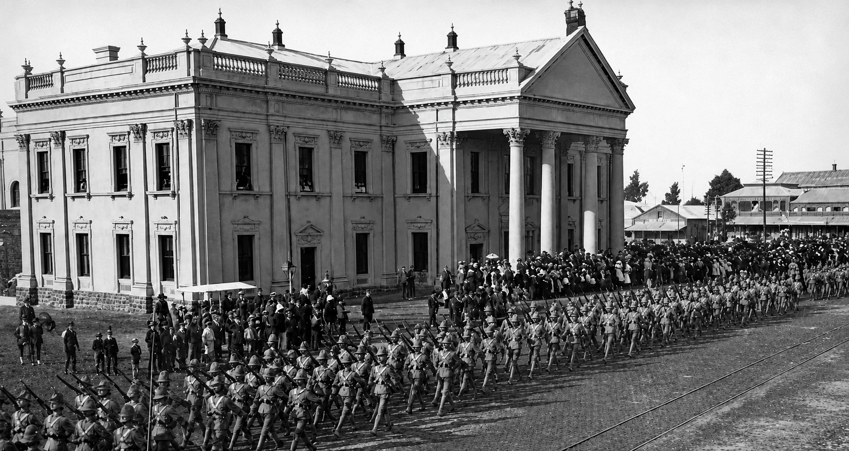 Historic black-and-white photograph of Kimberley Town Hall in September 1899, with a large formation of uniformed soldiers marching across the foreground and crowds gathered outside the newly completed Victorian building. The Post Office and other early Kimberley buildings are visible in the background.