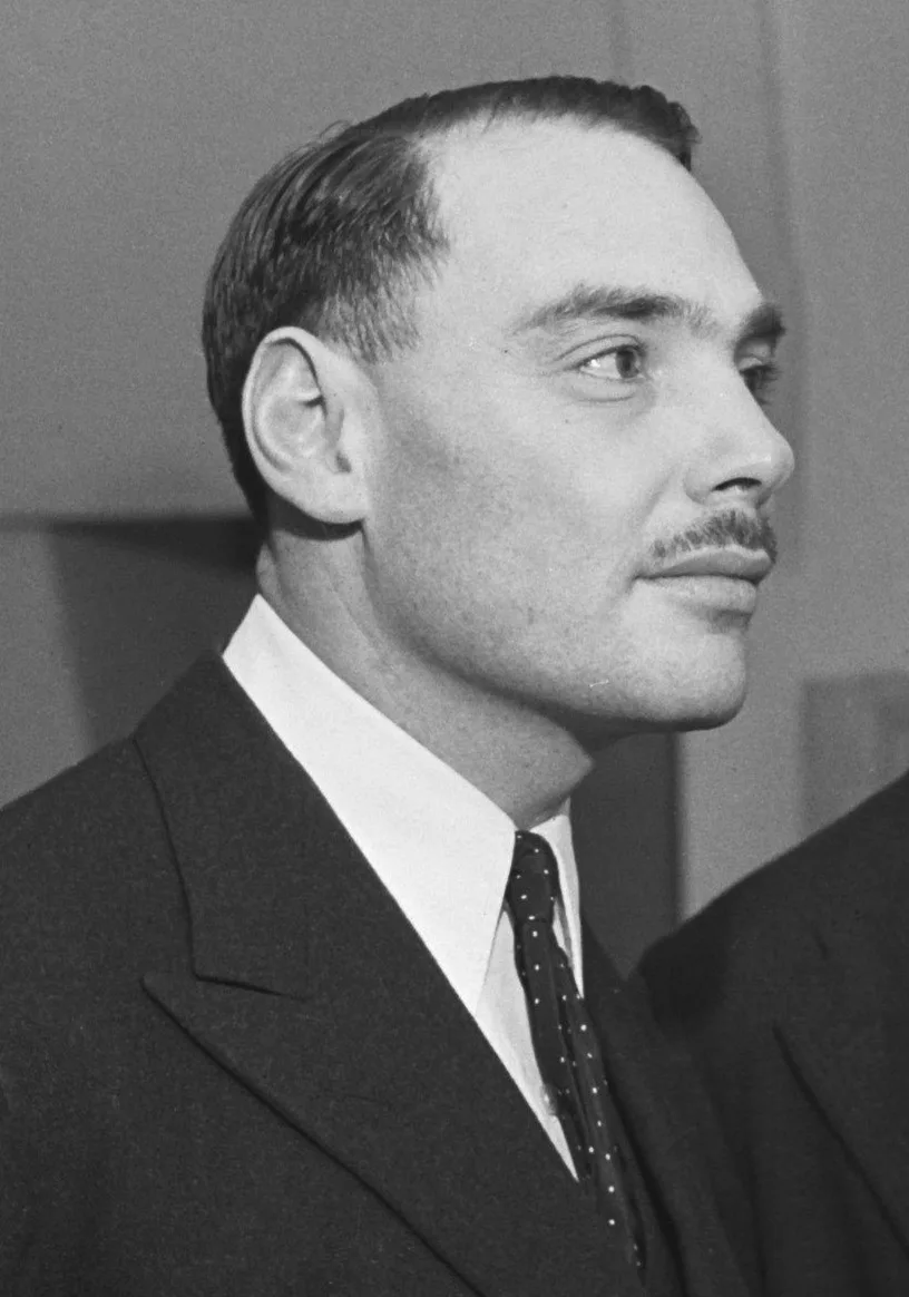 Black-and-white portrait of a young Harry Oppenheimer wearing a suit, tie and round spectacles in Amsterdam in 1945.