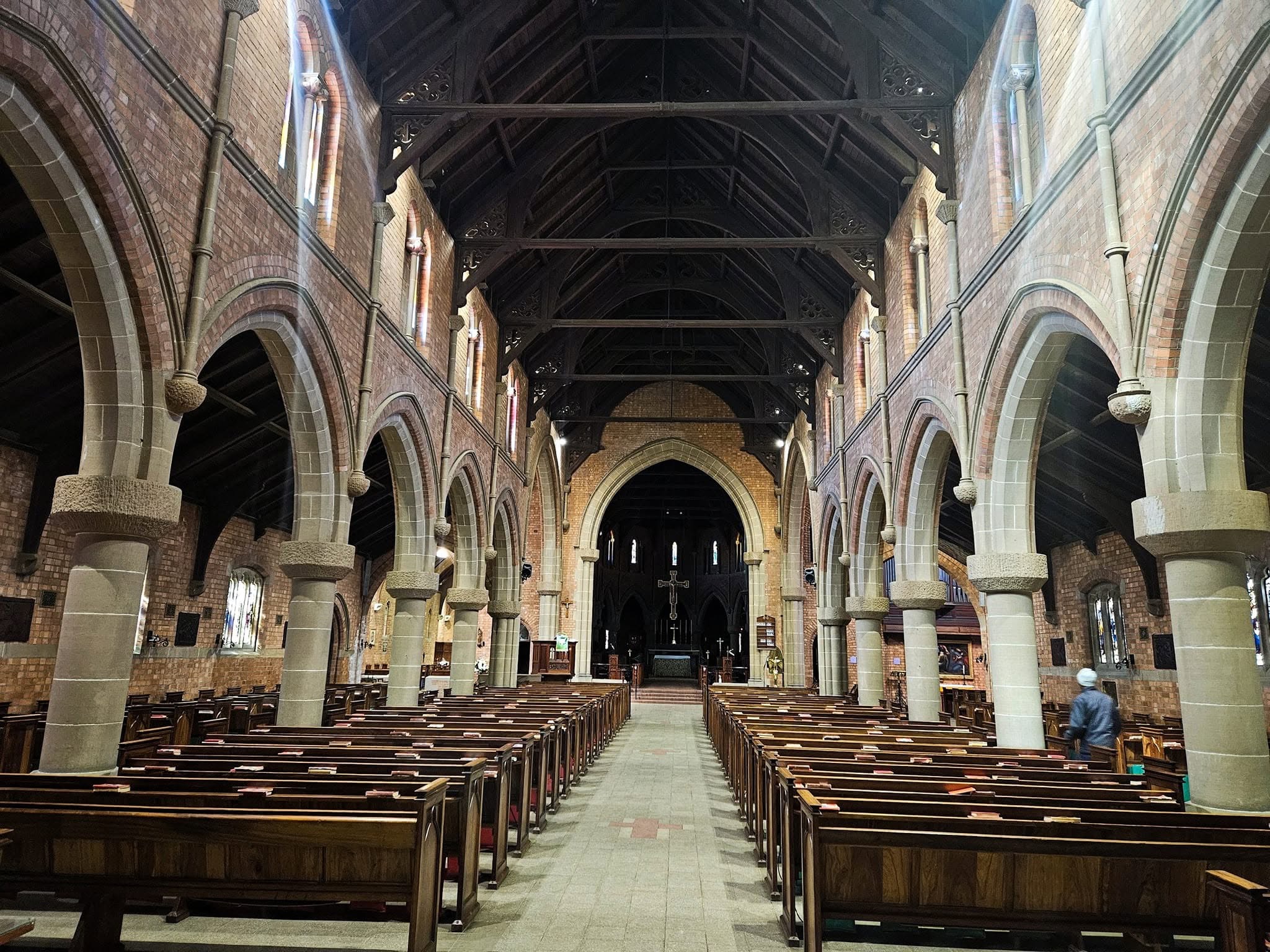Interior of St Cyprian's Cathedral in Kimberley, showing the long Gothic Revival nave, stone arcades, timber roof trusses and rows of wooden pews leading to the high altar.