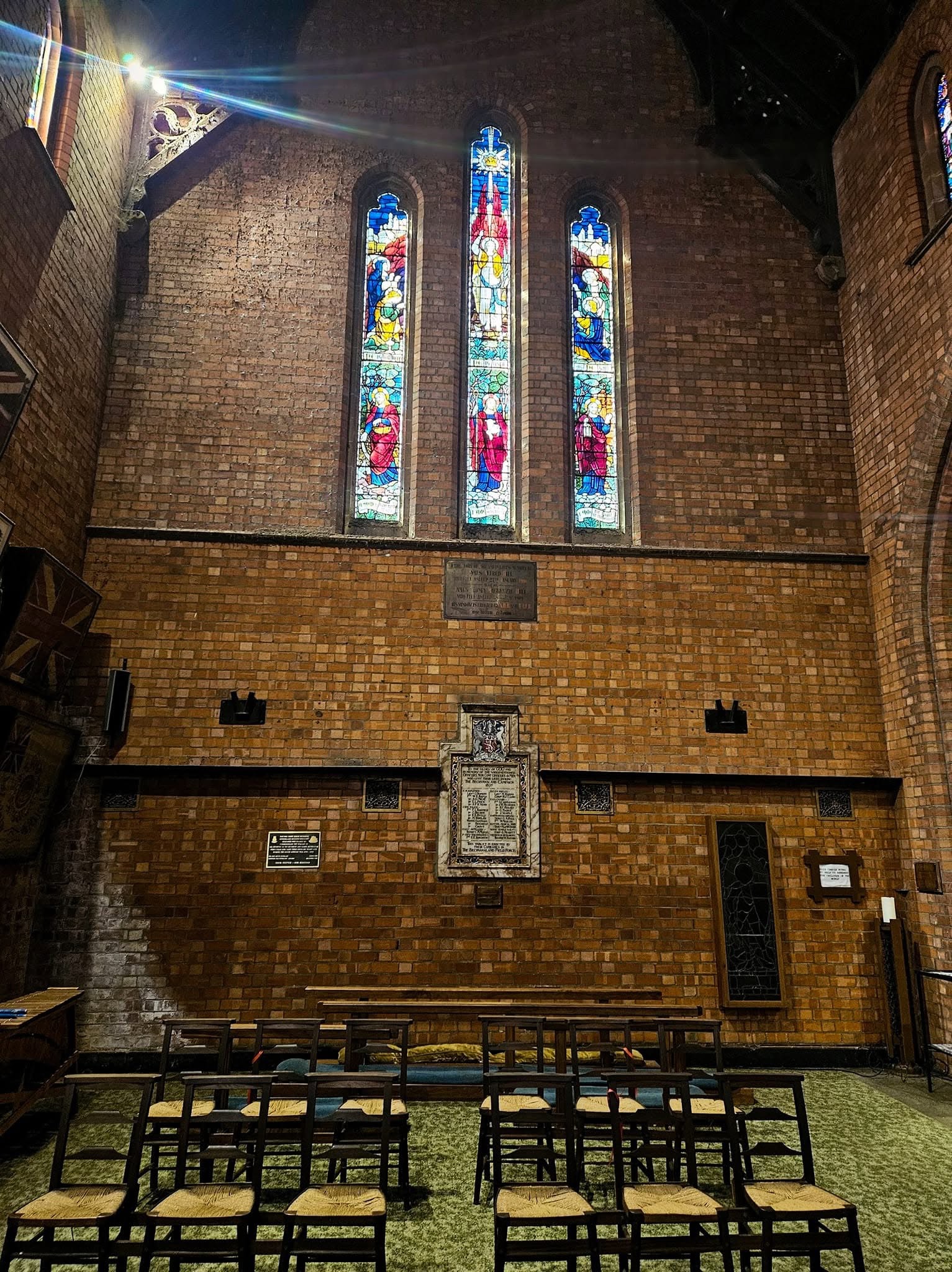 Stained-glass windows and memorial plaques at the east end of St Cyprian's Cathedral in Kimberley, illuminated by natural light.