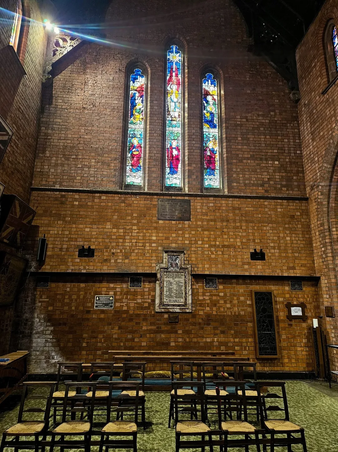 Stained-glass windows and memorial plaques at the east end of St Cyprian's Cathedral in Kimberley, illuminated by natural light.