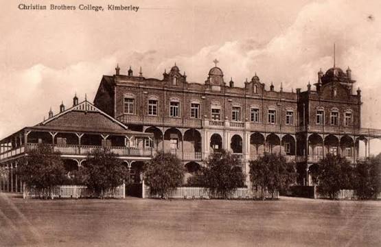 Historic sepia postcard showing Christian Brothers’ College Kimberley, with the long brick main building, arcaded verandas, tower and early campus structures.
