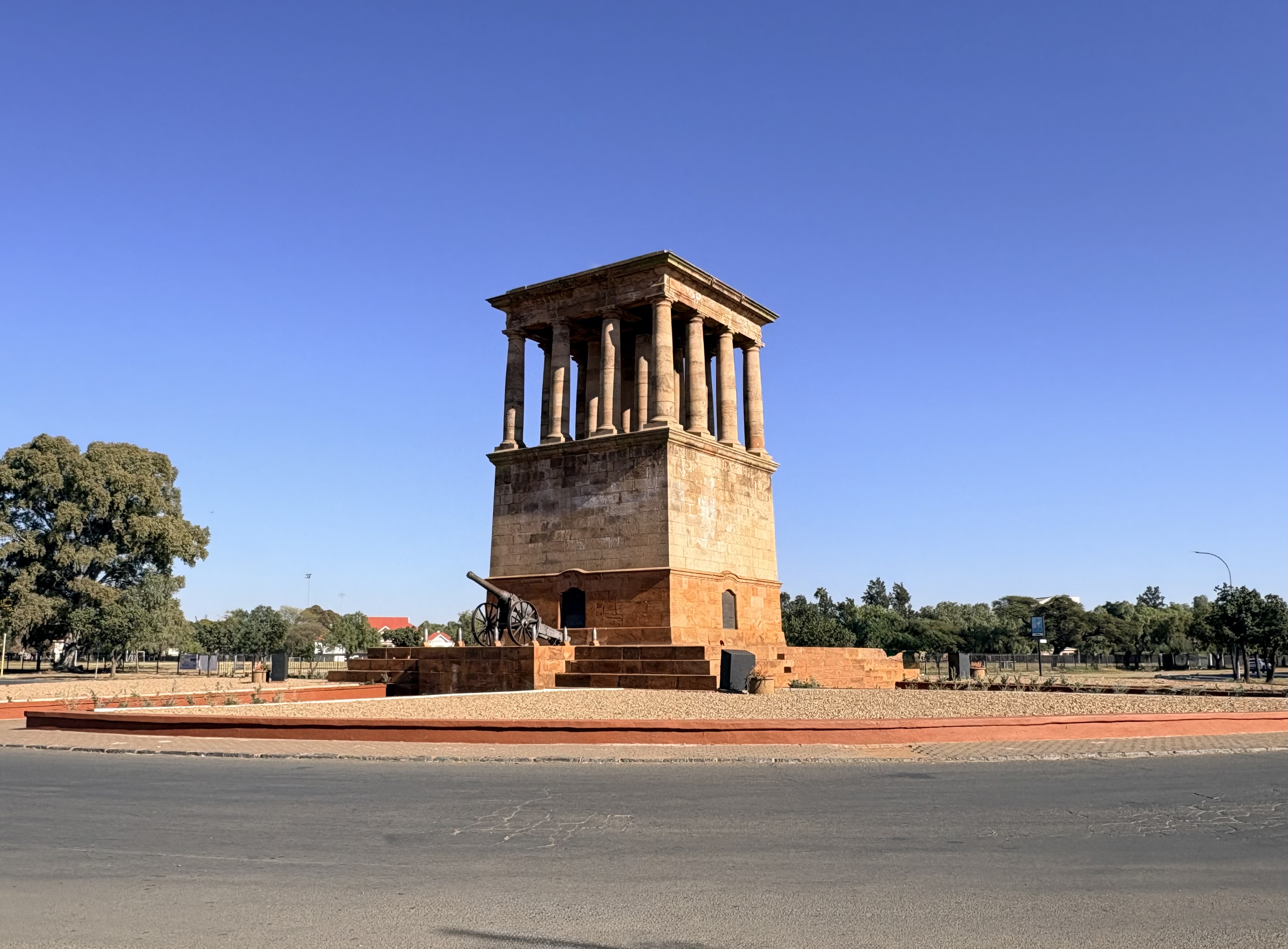 The Honoured Dead Memorial in Kimberley, Northern Cape, South Africa, designed by Sir Herbert Baker and unveiled in 1904, with Long Cecil displayed on the sandstone stylobate beneath the classical colonnade.