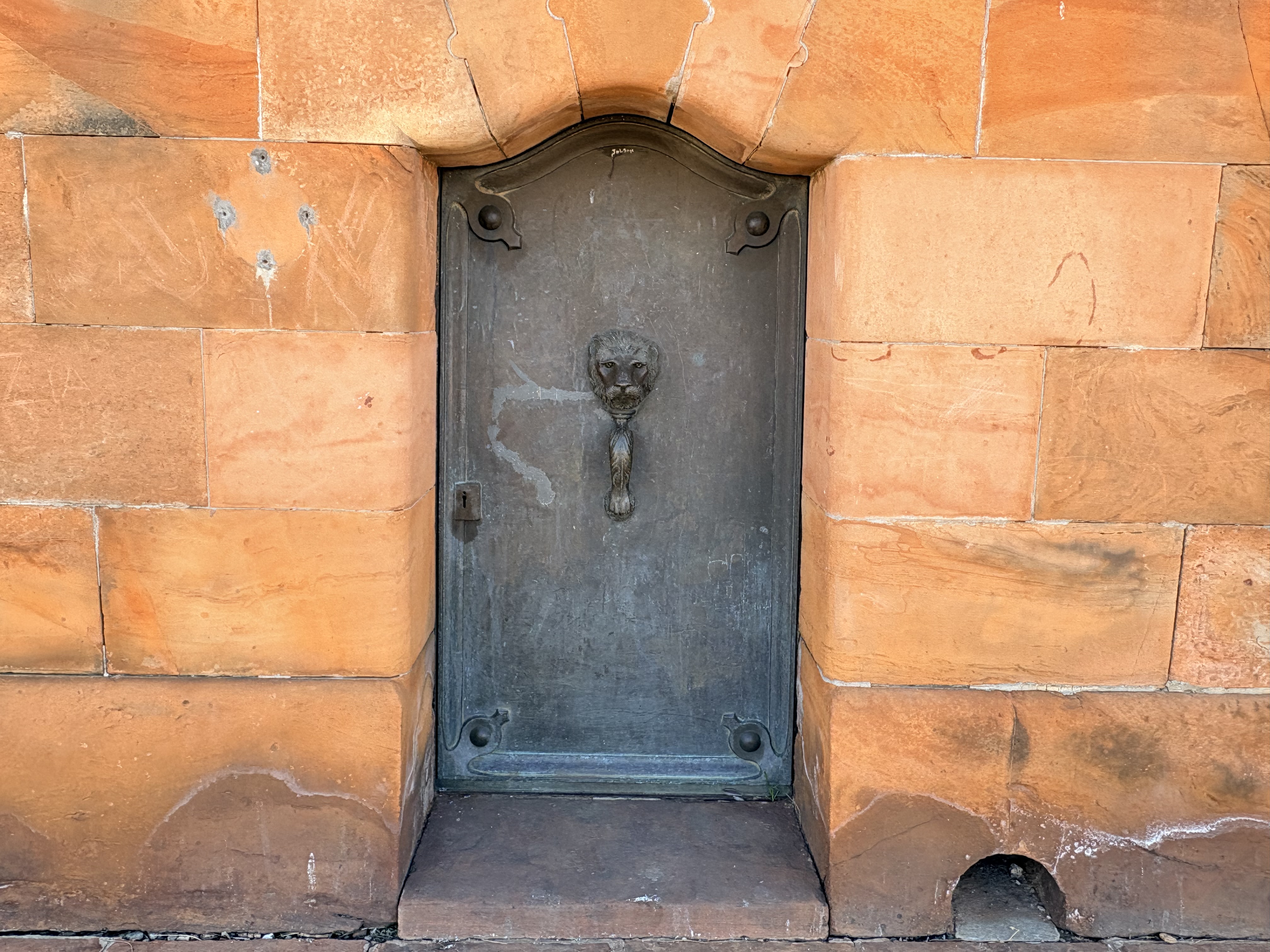 Bronze entrance door with an ornate lion-head handle leading to the crypt beneath the Honoured Dead Memorial in Kimberley.