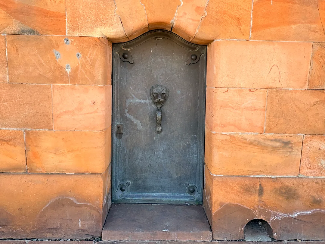Bronze entrance door with an ornate lion-head handle leading to the crypt beneath the Honoured Dead Memorial in Kimberley.