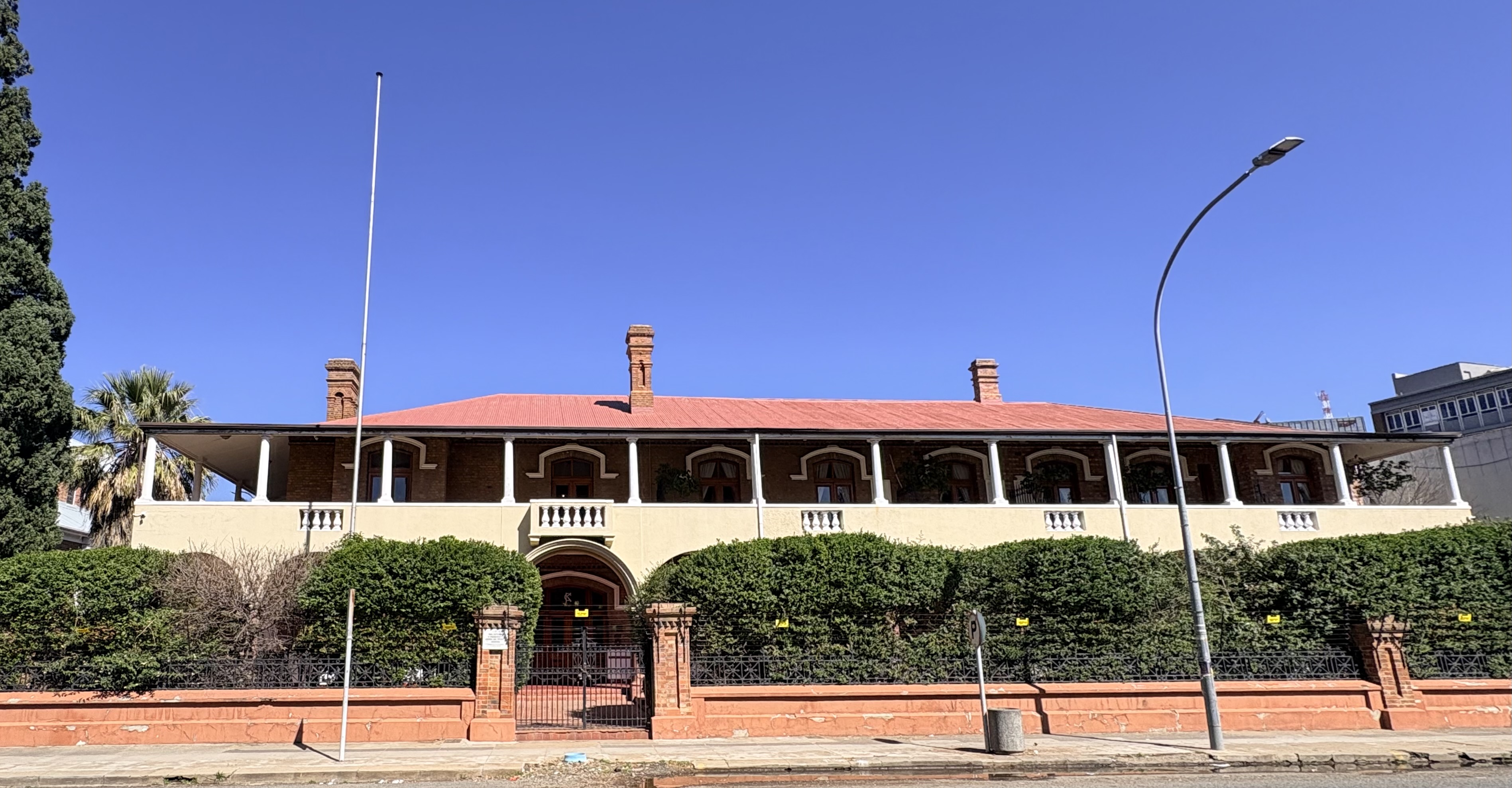 The Kimberley Club viewed from Du Toitspan Road in Kimberley, showing the historic two-storey frontage, verandahs, chimneys and former main entrance.