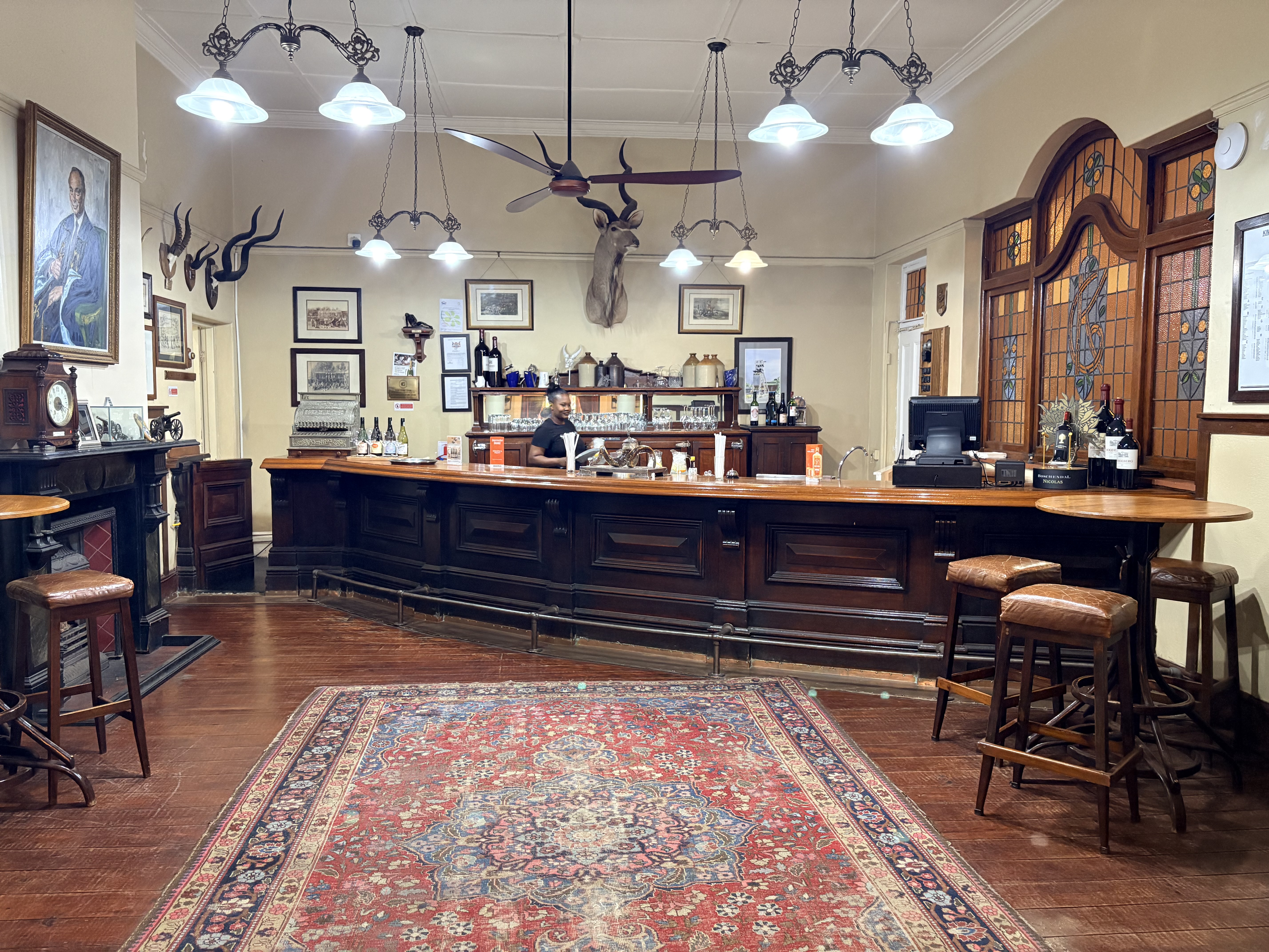 Historic timber bar at the Kimberley Club, with polished wood counter, high stools, stained-glass windows and traditional club furnishings.